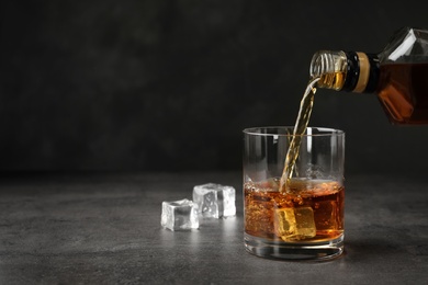 Pouring whiskey from bottle into glass with ice cubes on table. Space for text