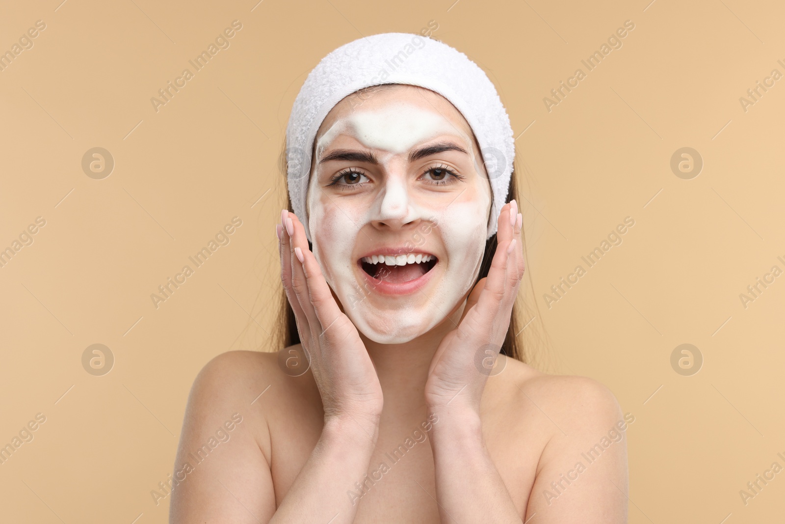 Photo of Young woman with headband washing her face on beige background