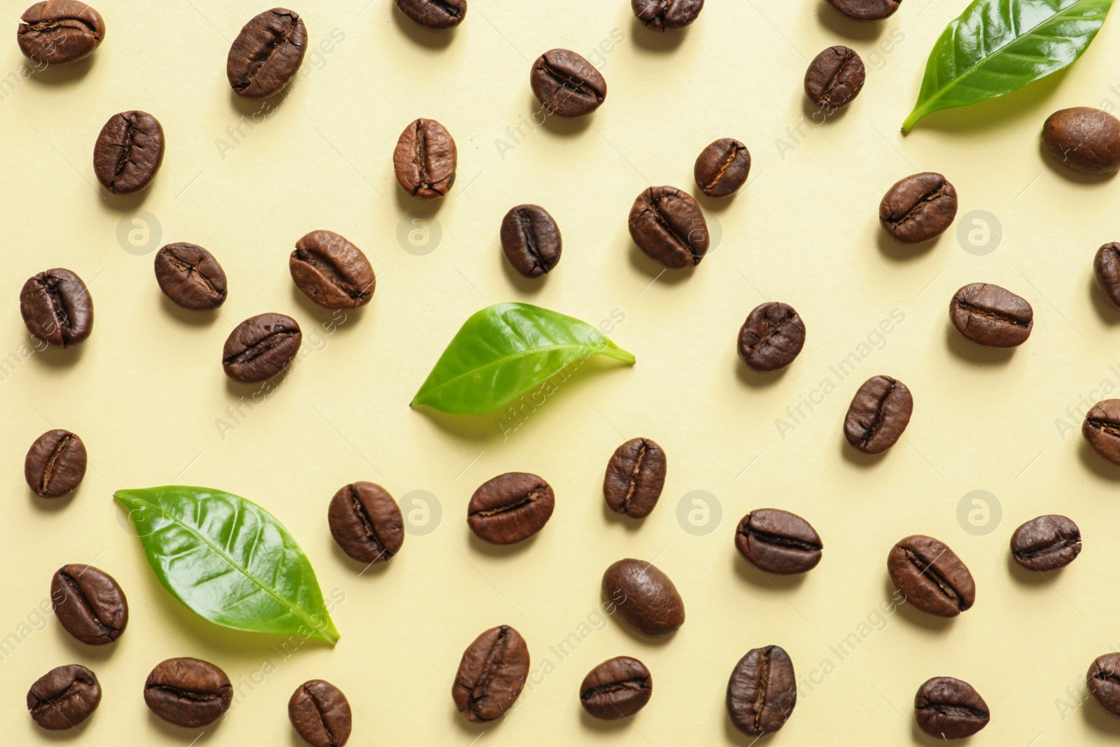 Photo of Fresh green coffee leaves and beans on light yellow background, flat lay