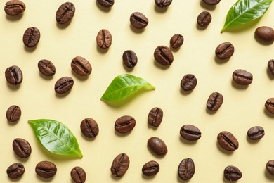 Fresh green coffee leaves and beans on light yellow background, flat lay