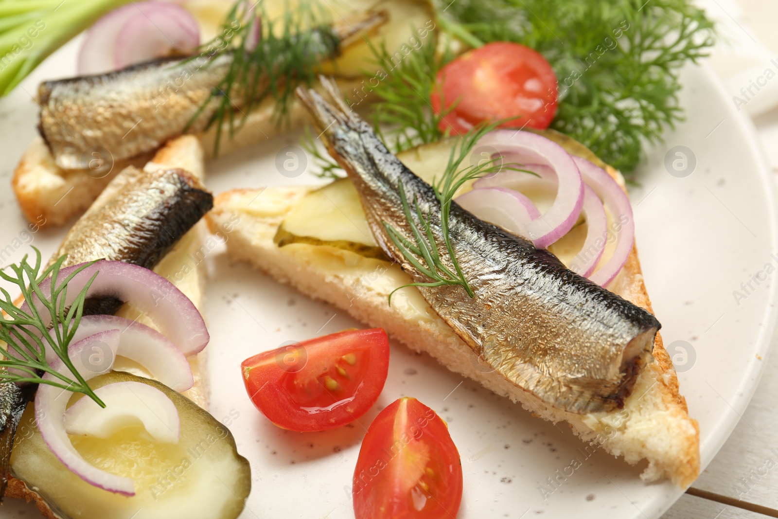 Delicious sandwiches with sprats, pickled cucumber, onion and dill served on white wooden table, closeup Photo of Delicious sandwiches with sprats, pickled cucumber, onion and dill served on white wooden table, closeup