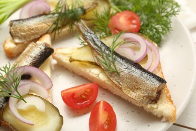 Photo of Delicious sandwiches with sprats, pickled cucumber, onion and dill served on white wooden table, closeup
