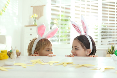 Cute children wearing bunny ears headbands at table with Easter eggs, indoors