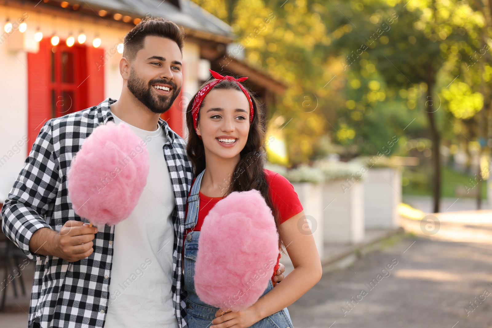 Photo of Happy couple with cotton candies outdoors, space for text