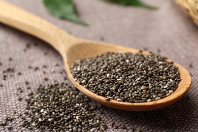 Wooden spoon with chia seeds on grey fabric, closeup
