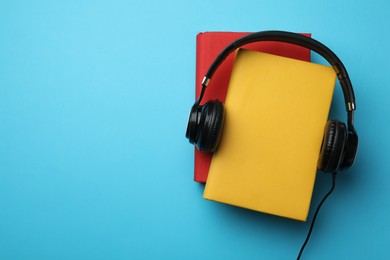 Photo of Books and modern headphones on light blue background, top view. Space for text