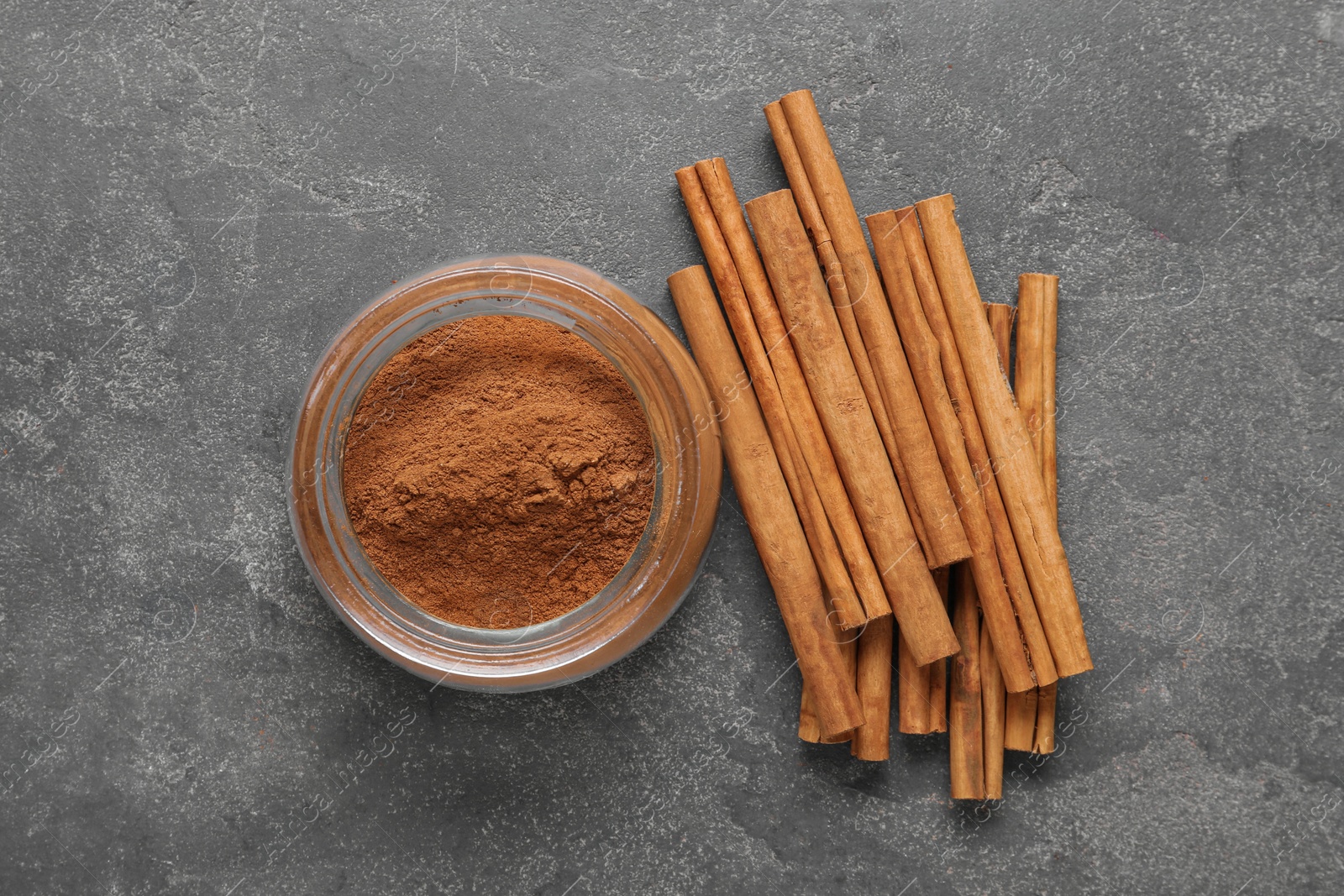 Photo of Aromatic cinnamon powder and sticks on grey table, flat lay