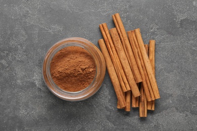 Aromatic cinnamon powder and sticks on grey table, flat lay