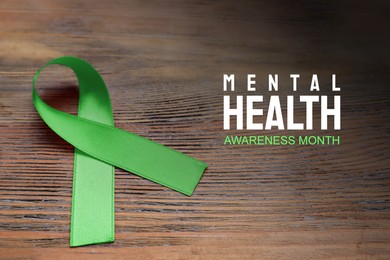 Image of World Mental Health Day. Green ribbon on wooden table, closeup view