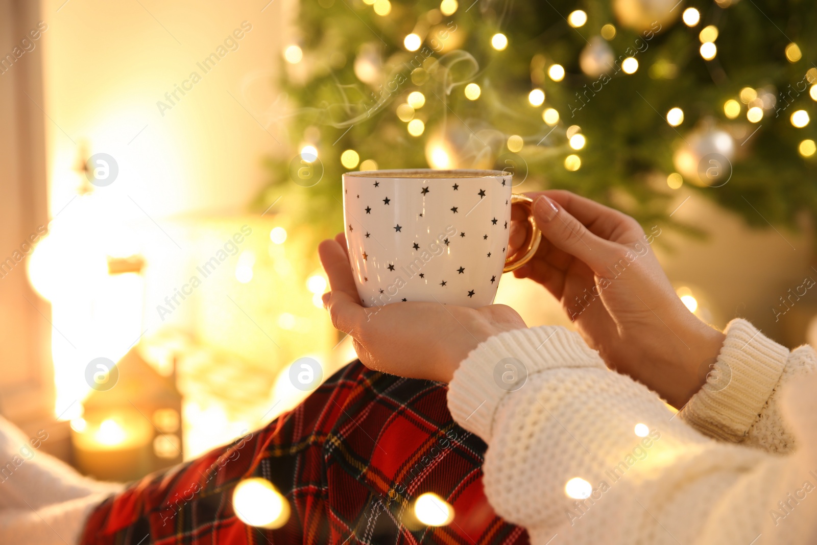 Photo of Woman with cup of hot drink near Christmas tree indoors, closeup