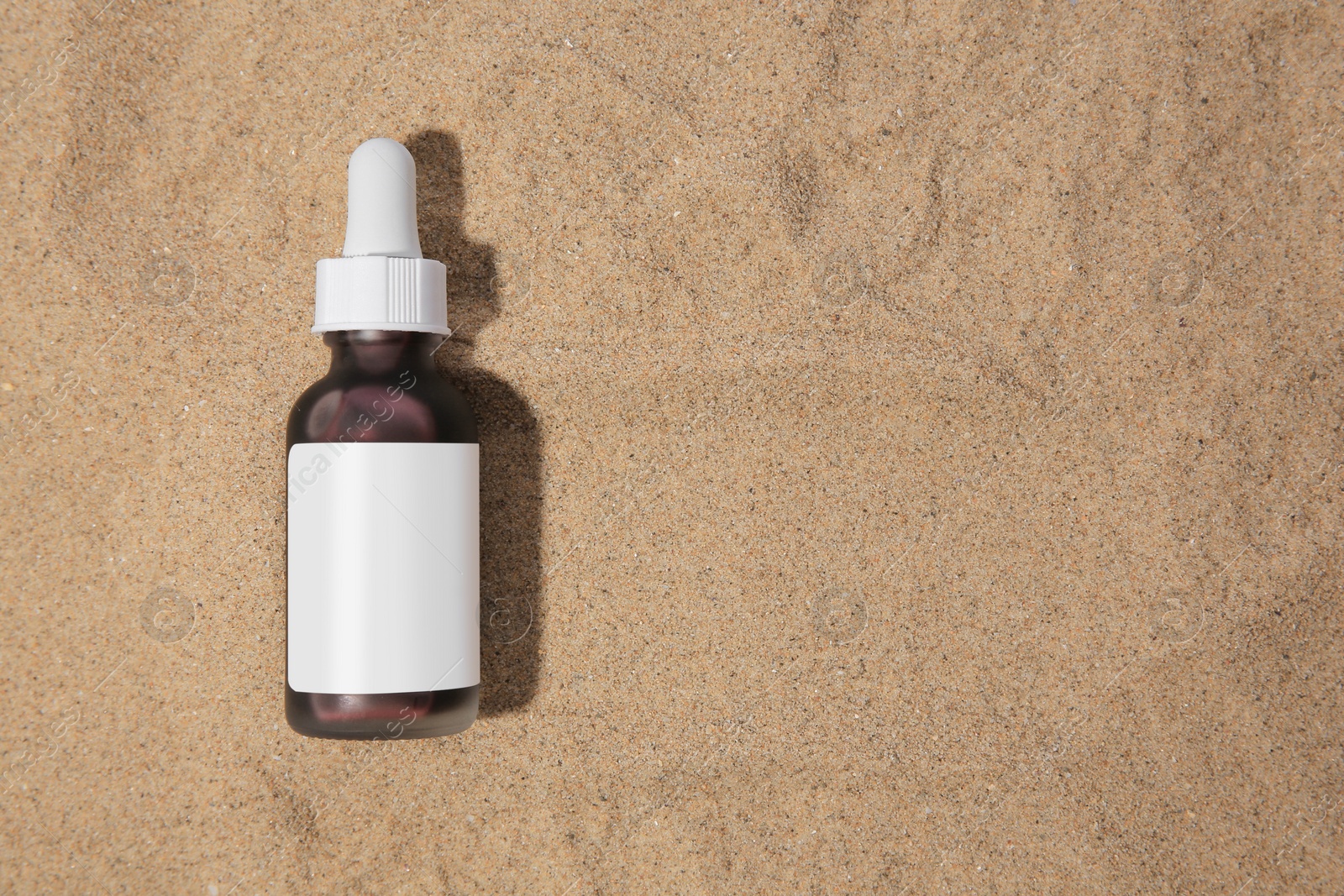 Photo of Bottle with serum on sand, top view and space for text. Cosmetic product