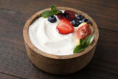 Bowl with yogurt, berries, fruits and mint on wooden table, closeup