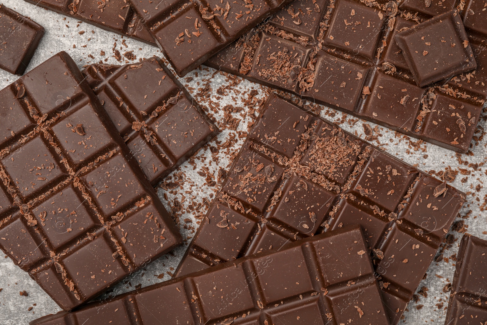 Photo of Pieces and shavings of tasty chocolate bars on light grey table, flat lay