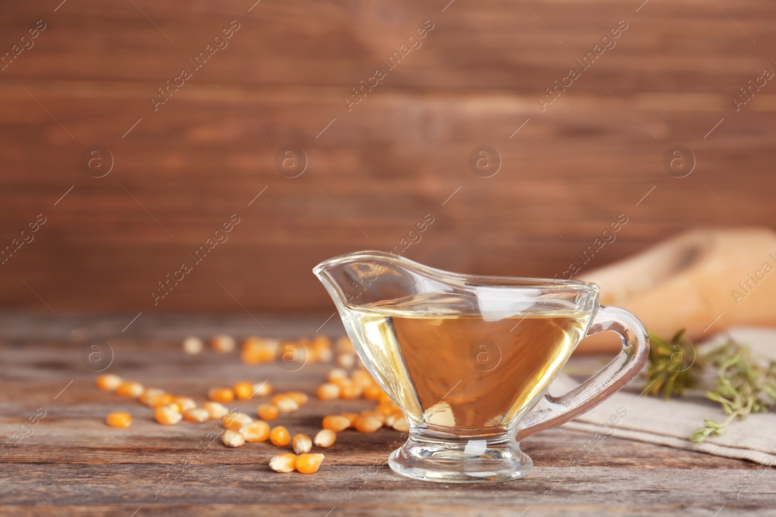 Photo of Gravy boat of corn oil and kernels on table against wooden wall