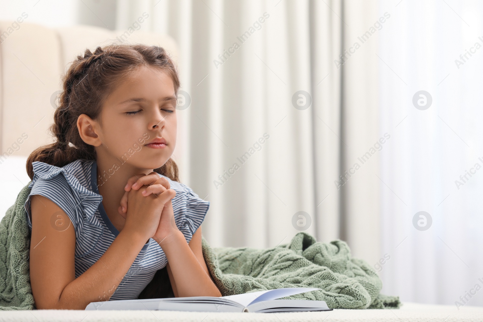 Photo of Cute little girl praying over Bible in bedroom