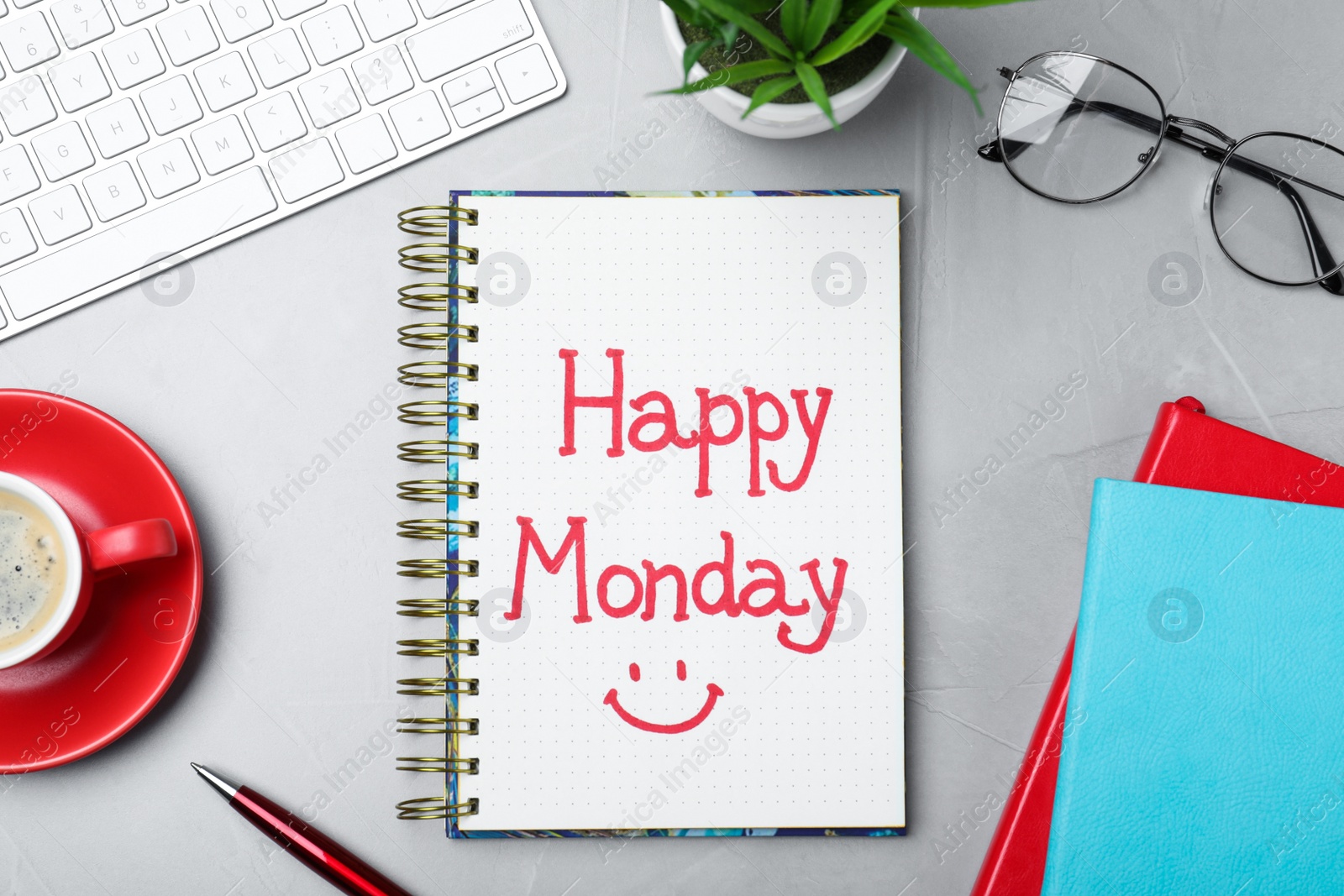 Photo of Message Happy Monday written in notebook, office stationery and cup of coffee on light desk, flat lay