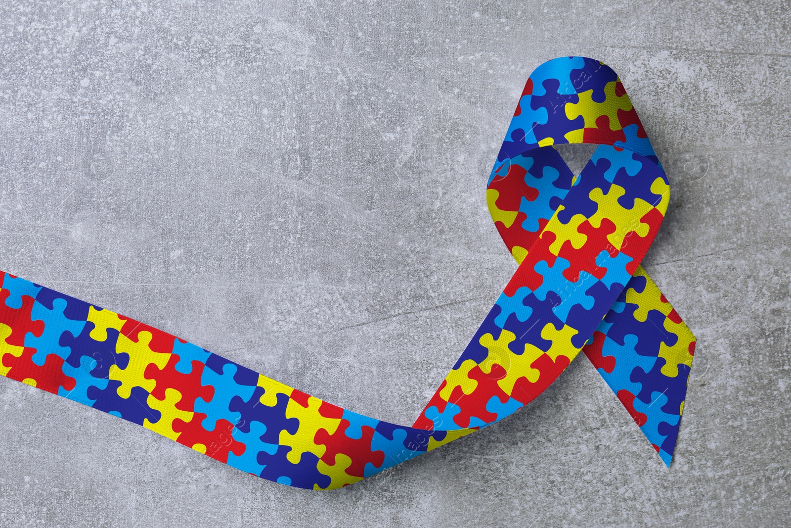 Image of World Autism Awareness Day. Colorful puzzle ribbon on light grey stone background, top view