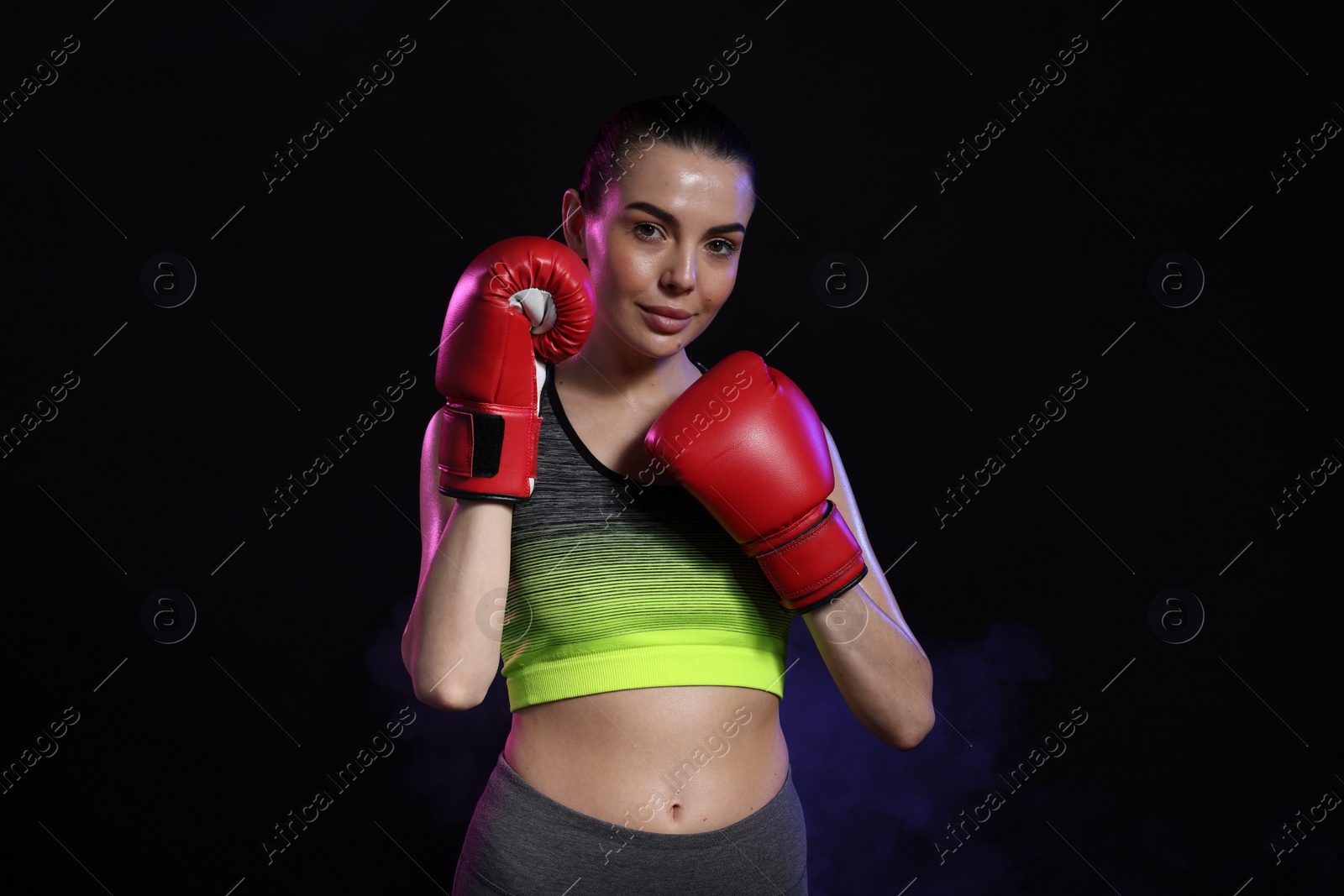 Photo of Portrait of beautiful woman wearing boxing gloves in color lights on black background