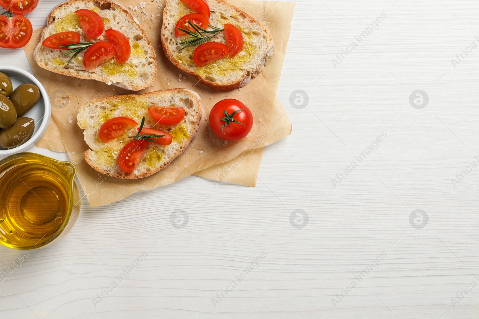 Photo of Tasty bruschettas with oil, tomatoes and rosemary on white wooden table, flat lay. Space for text