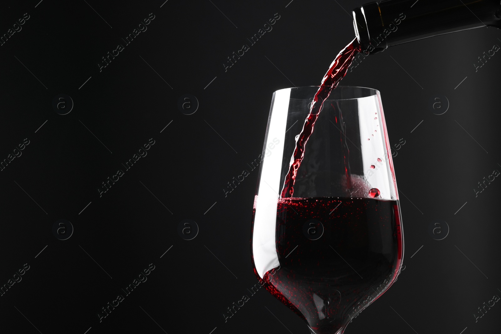 Photo of Pouring red wine into glass against black background, closeup. Space for text