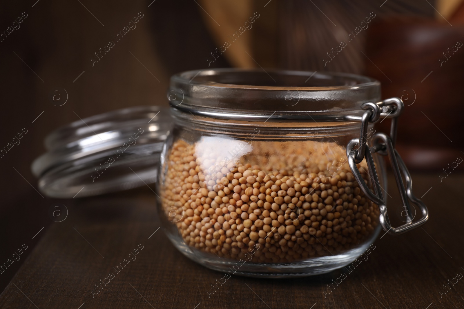 Photo of Mustard seeds in glass jar on wooden table, closeup