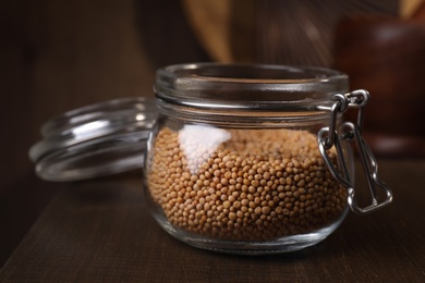 Photo of Mustard seeds in glass jar on wooden table, closeup