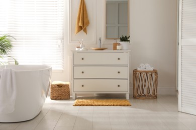 Photo of Stylish orange mat near chest of drawers in bathroom