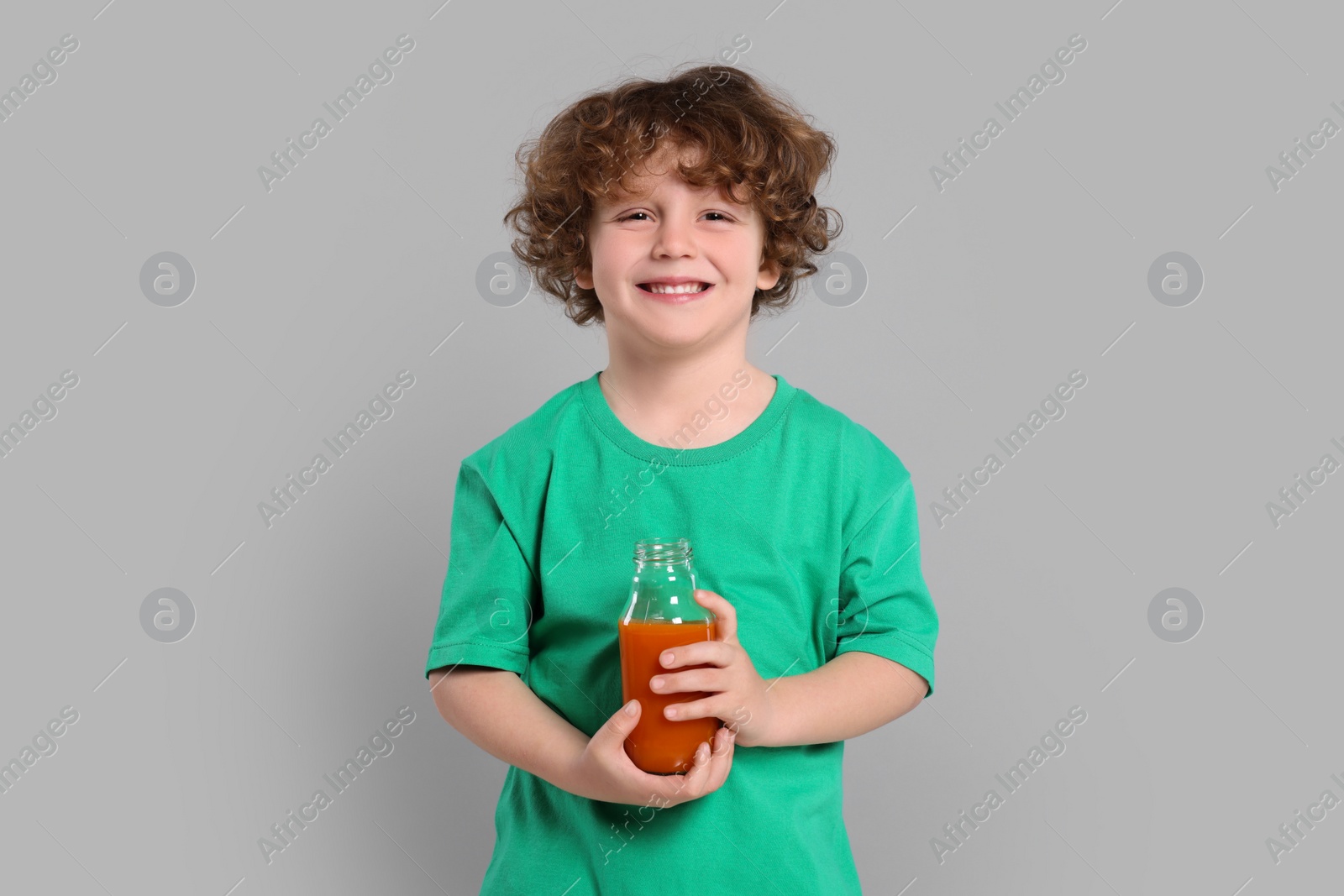 Photo of Cute little boy with glass bottle of fresh juice on light gray background