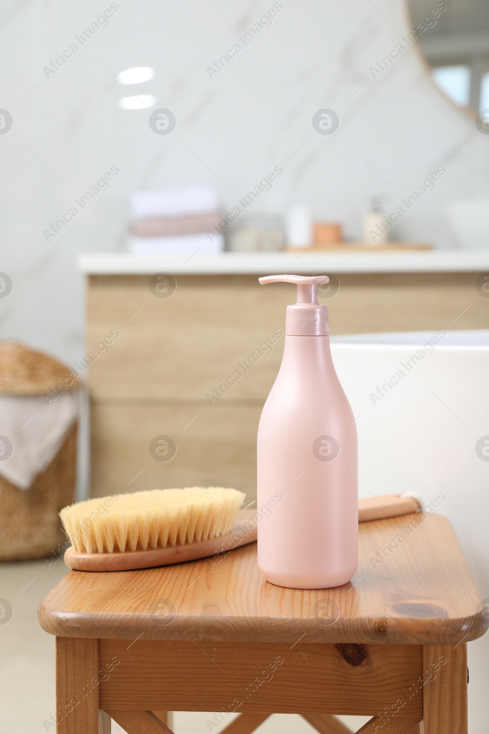 Photo of Bottle of shower gel and brush on wooden table near tub in bathroom