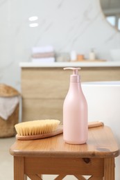 Bottle of shower gel and brush on wooden table near tub in bathroom