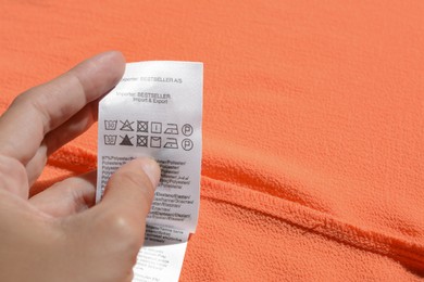 Photo of Woman holding clothing label on coral garment, closeup. Space for text