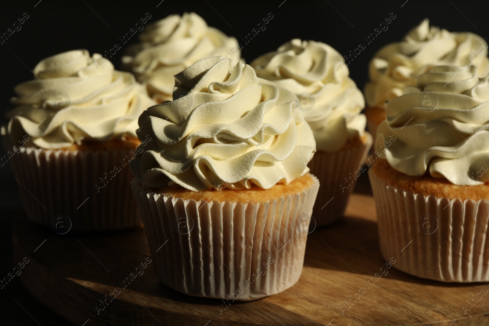 Photo of Tasty cupcakes with vanilla cream on wooden stand, closeup