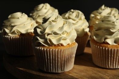 Photo of Tasty cupcakes with vanilla cream on wooden stand, closeup