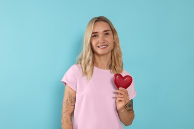 Photo of Happy volunteer holding red heart with hands on light blue background