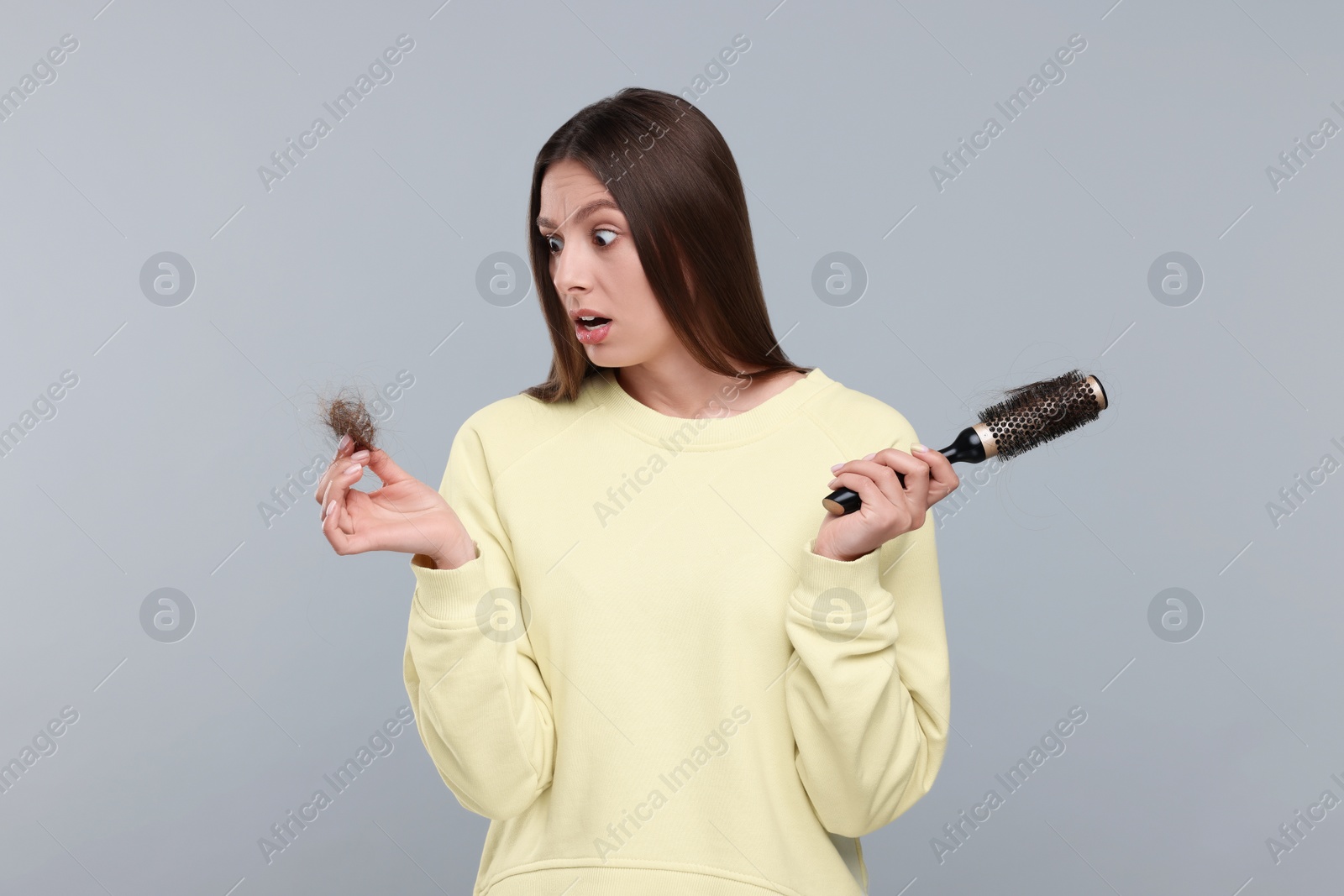 Photo of Emotional woman holding brush with lost hair on light grey background. Alopecia problem