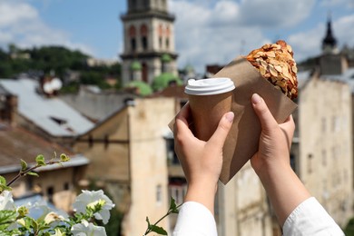 Photo of Woman with delicious croissant and paper cup of coffee outdoors, closeup. Space for text