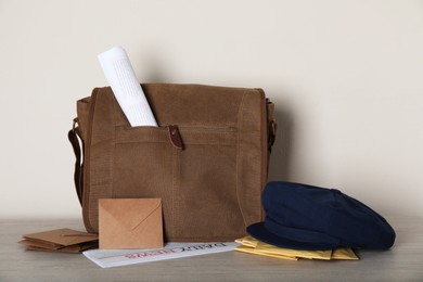 Postman's hat near bag with letters and newspapers on wooden background