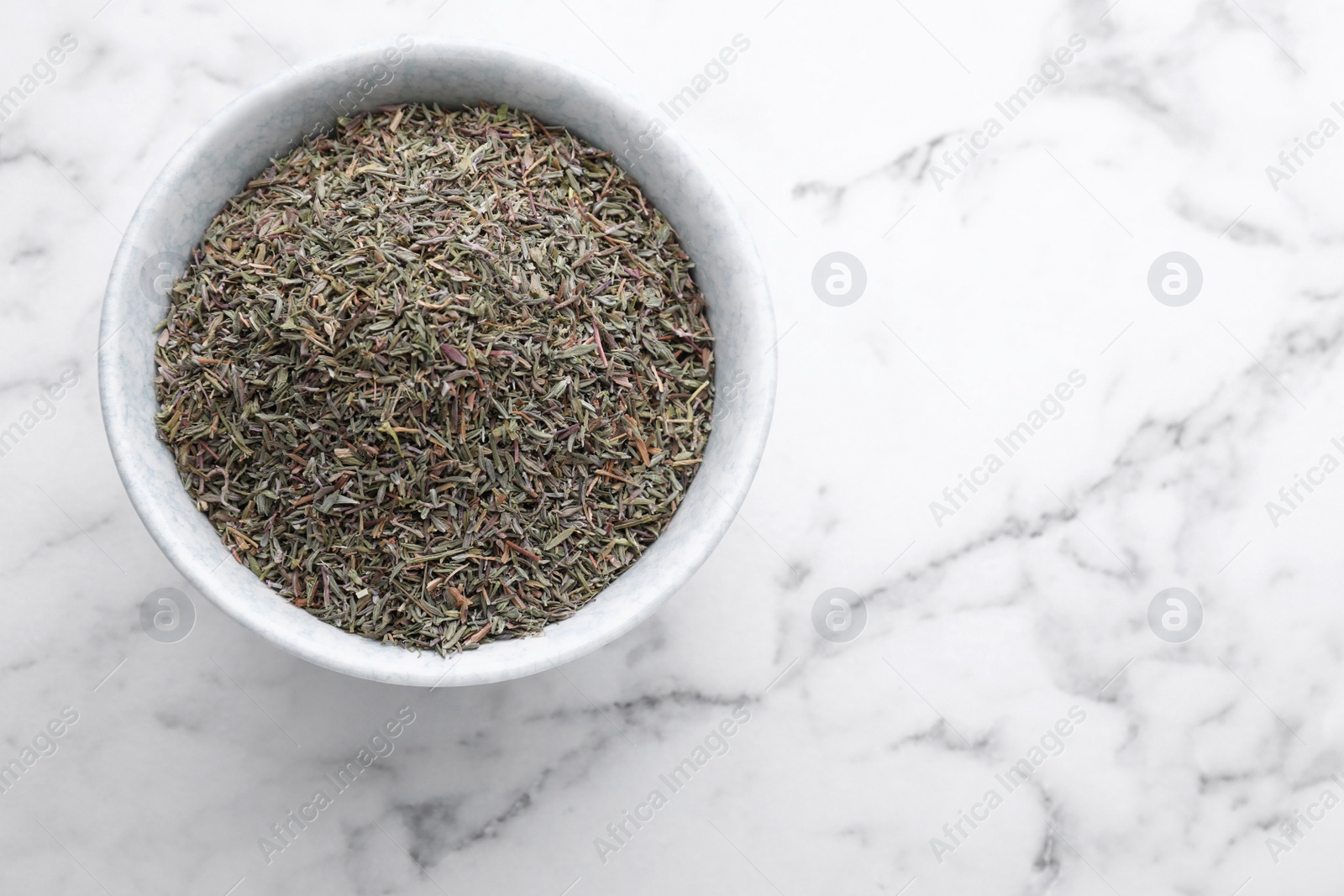 Photo of Bowl with dried thyme on white marble table, top view. Space for text