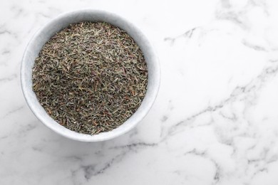 Photo of Bowl with dried thyme on white marble table, top view. Space for text