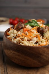 Delicious pilaf with meat and carrot in bowl on wooden board, closeup