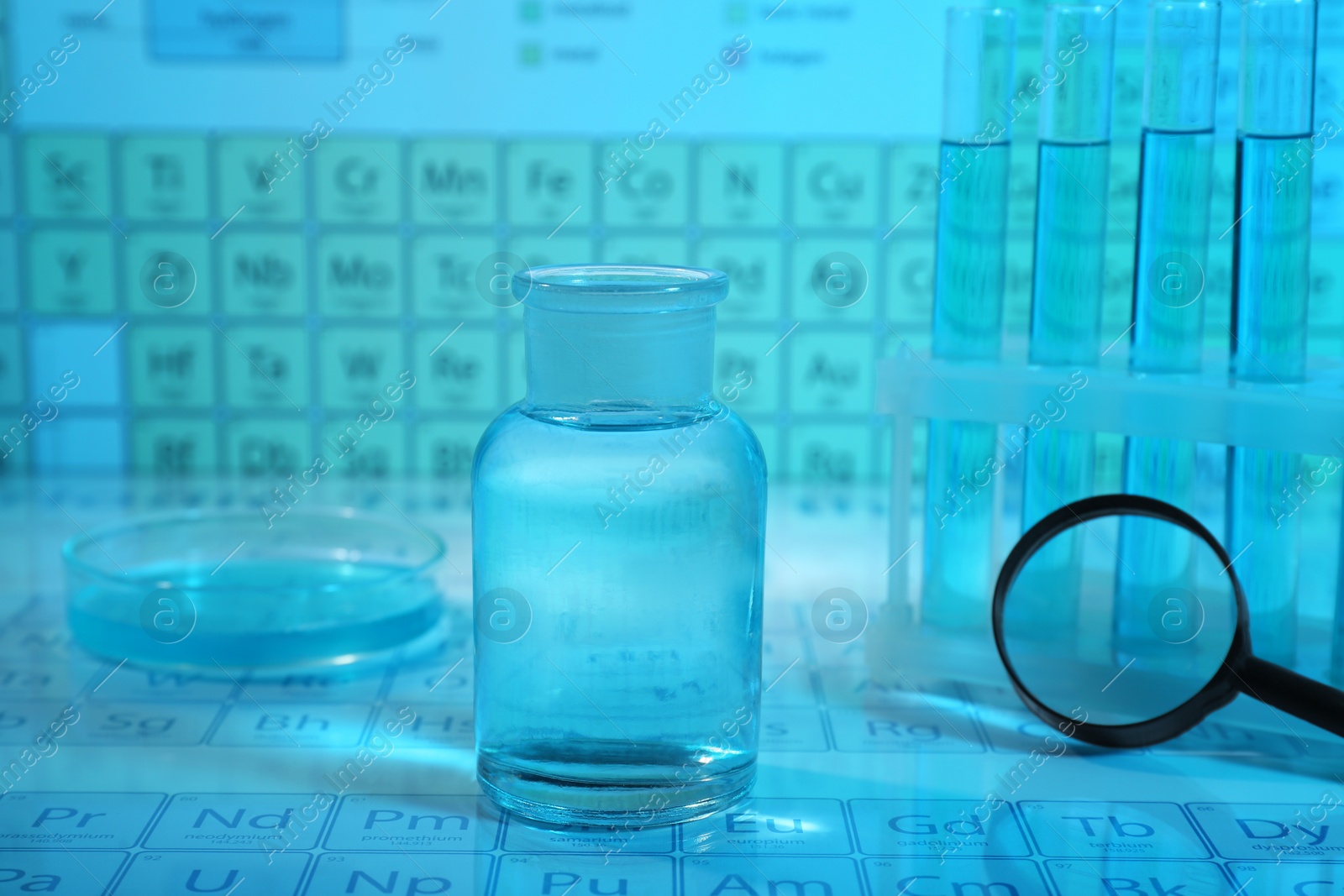 Photo of Laboratory glassware, petri dish and magnifying glass on periodic table of elements, closeup. Color tone effect