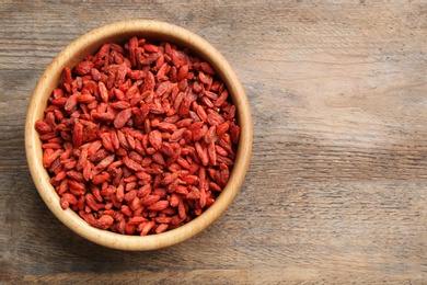 Photo of Bowl of dried goji berries on wooden table, top view with space for text. Healthy superfood