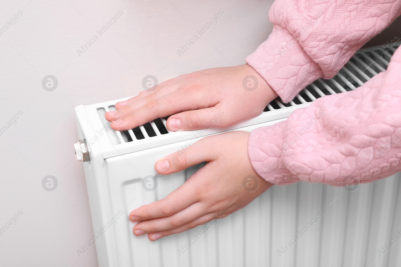 Photo of Girl warming hands on heating radiator indoors, closeup