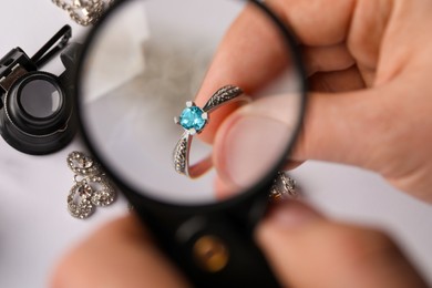 Photo of Jeweler examining topaz ring with magnifying glass at white table, closeup