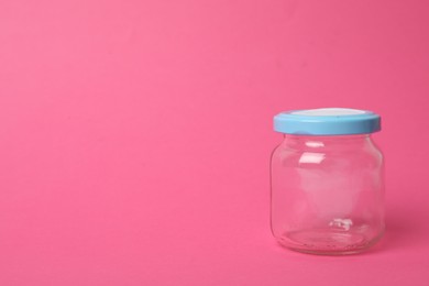 Closed empty glass jar on pink background, space for text