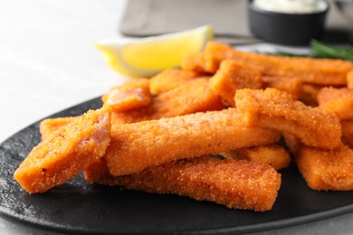 Photo of Tasty fresh fish fingers on black plate, closeup