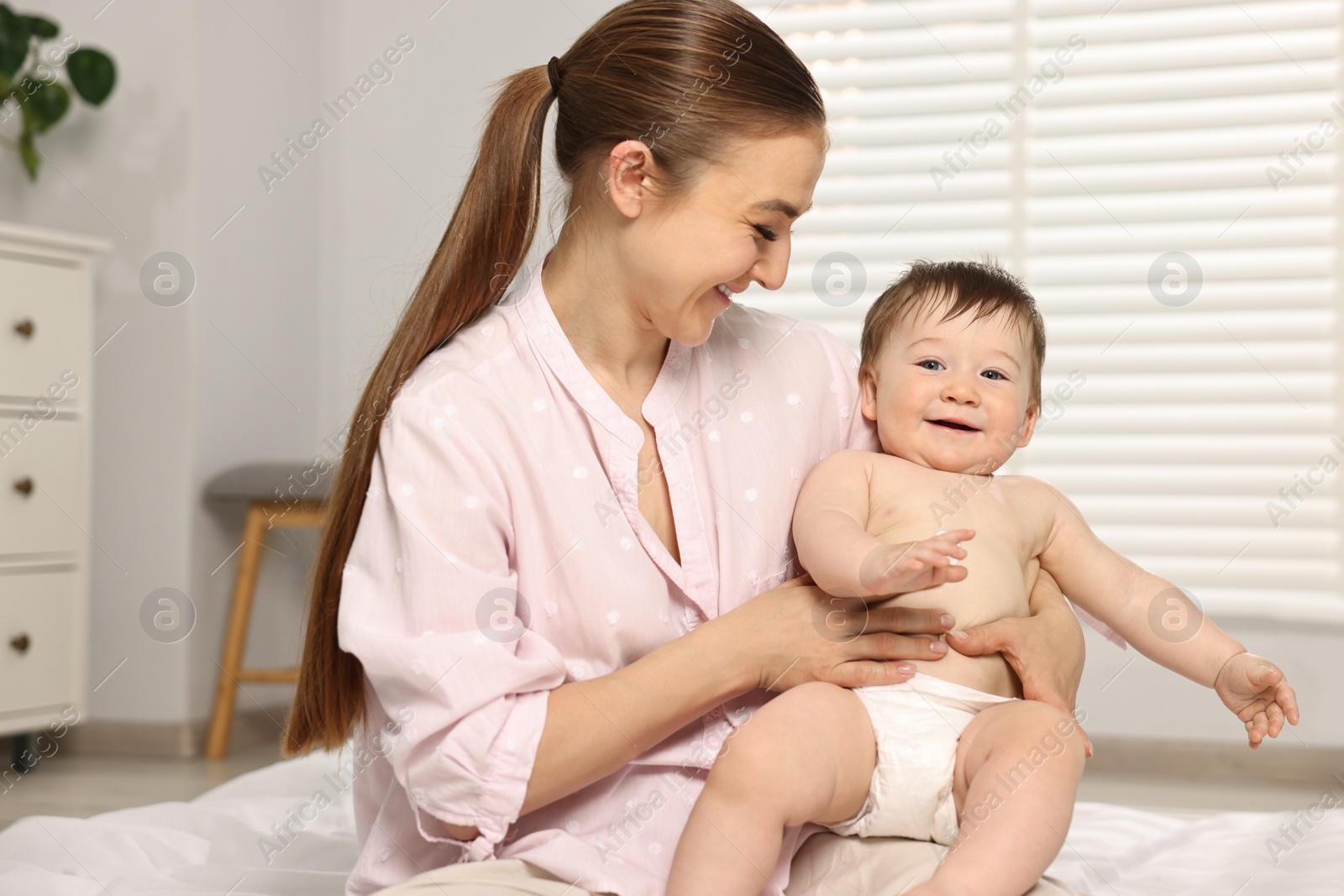 Photo of Happy mother applying body cream onto baby`s skin at home