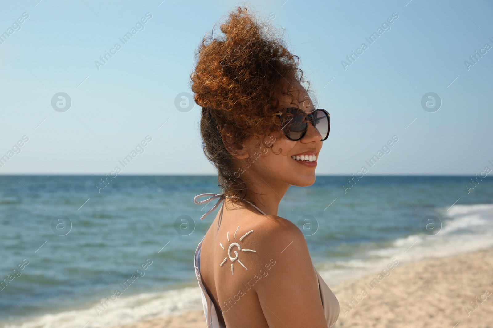 Photo of Beautiful African American woman with sun protection cream on shoulder at beach