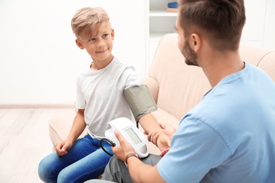 Young man checking little boy's pulse indoors