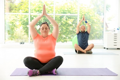 Photo of Overweight man and woman practicing yoga in gym